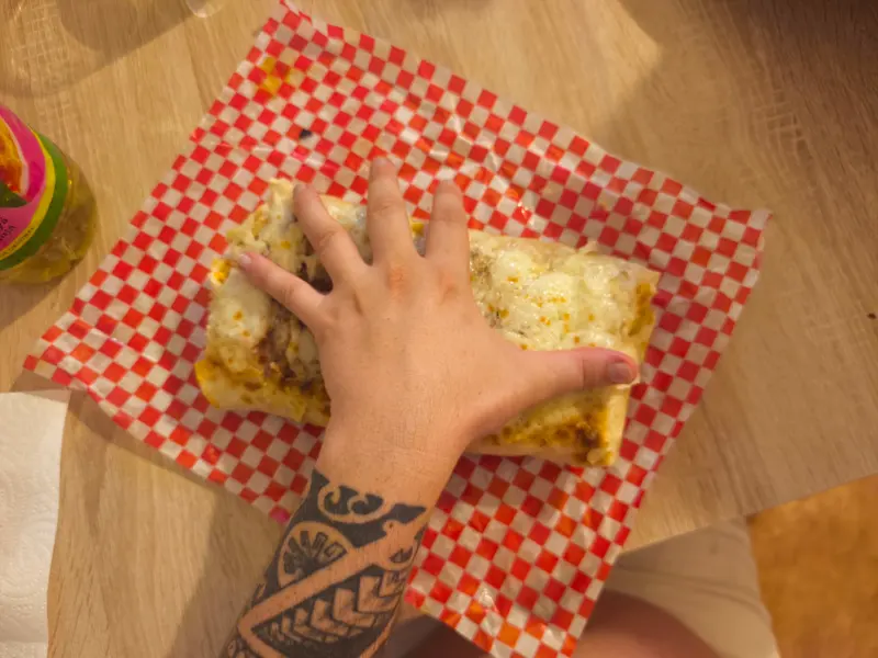 Un cliente sujeta un french taco gratinado recién hecho sobre papel de cuadros rojo y blanco