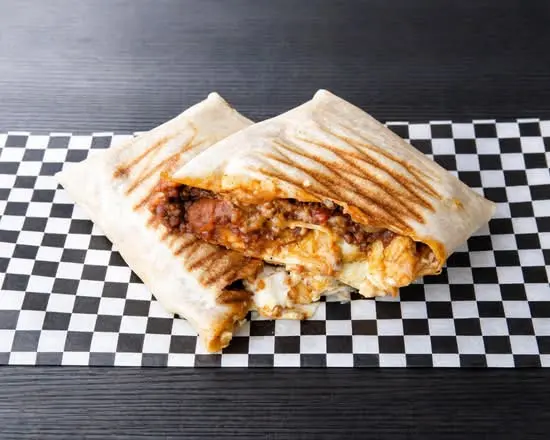 Taco El Rancho partido en dos sobre papel de cuadros, con tenders de pollo, barbacoa y queso fundido